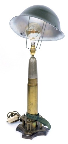 A military style table lamp, comprising a shell case converted to table lamp on a tripod base with applied miniature empty shells and a tin helmet shade, 72cm high.