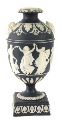 A Wedgwood black basalt urn, on black ground with white dancing figures on a stepped foot lacking cover, 18cm high. (AF)