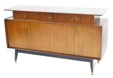 A mid century teak sideboard, with a raised top with arrangement of three drawers, two cupboard doors, on ebonised brass capped tapering legs, 85cm high, 148cm wide, 46cm deep.