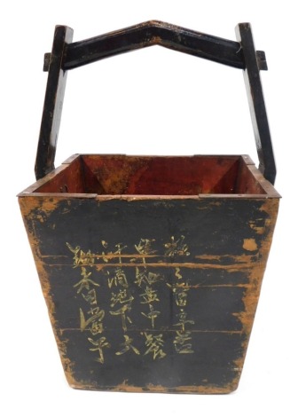 An Oriental ebonised log basket, with a shaped handle on square set bucket base, painted black with Oriental script, 73cm high, the bucket 38cm x 38cm.