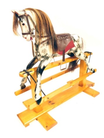 A dapple grey rocking horse, with burgundy leatherette saddle, on a pine base, 121cm long.