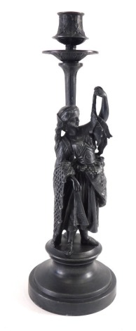 A spelter candlestick, elaborately decorated, with shaped dish holder on shaped stem, fronted by a figure dressed in finery, on an inverted socle, 33cm high.