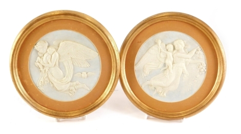 A pair of moulded pressed paper plaques, each decorated with angels, children, etc., in gilt frames, 22cm diameter overall.