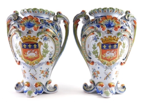 A pair of continental tin glazed armorial vases, each marked Havre profusely decorated with raised scroll and shell pattern, decorated with coats of arms and flanked by scroll handles on shaped feet, 32cm high. (2)