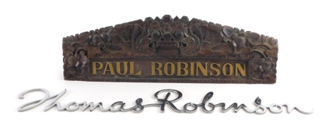 An elaborately carved door plaque, signed Paul Robinson, 36cm wide, and a script chrome finish signed Thomas Robinson. (2)