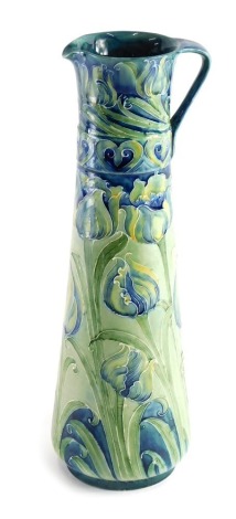 An early 20thC Moorcroft Liberty Florian ware jug, of tapering cylindrical form, decorated with flowers in green and blue, signature and printed marks beneath, 31cm high.