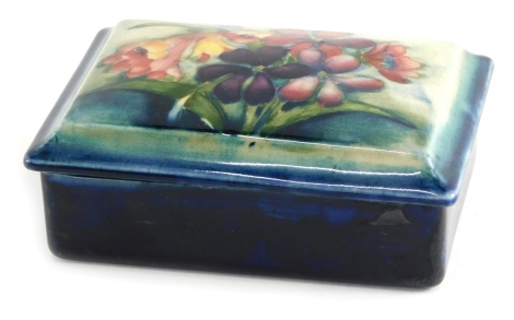 A mid 20thC Moorcroft Spring Flowers and Orchid pattern box and cover, of rectangular form on blue ground, impressed and signature marks beneath, 13cm wide.