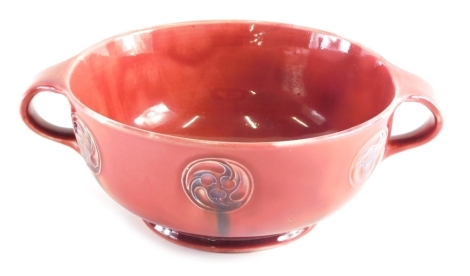 An early 20thC Moorcroft Liberty and Co Red Flaminian ware bowl, of circular form with moulded handles, on circular foot, impressed marks and signature mark beneath, 24cm wide.