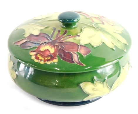 A Moorcroft Orchid pattern jar and cover, of circular form on green ground, impressed marks beneath, 11cm diameter.