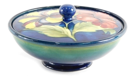 A 20thC Moorcroft Hibiscus pattern jar and cover, of circular form with removable lid, on blue ground, impressed marks with label beneath, 17cm diameter.